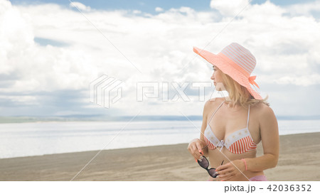 Attractive woman in a hat stands on the beach against the blue sea. 42036352