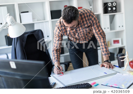 A man in the office is standing near the table and draws a marker on the magnetic board. A man in the office is standing near the table and draws a marker on the magnetic board. 42036509