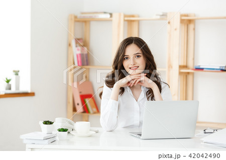 Smiling young woman sitting in front of notebook in the office. 42042490