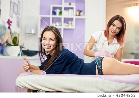 Attractive female massage professional is giving massage to a beautiful smiling female client of a Attractive female massage professional is giving massage to a beautiful smiling female client of a 42044855