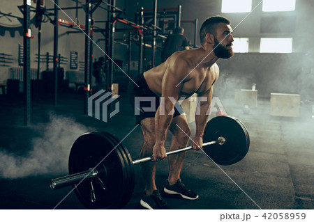 Fit young man lifting barbells working out in a gym 42058959