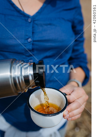 Woman pouring hot tea from a thermos on a sandy beach on a Sunny day. Close up. Woman pouring hot tea from a thermos on a sandy beach on a Sunny day. Close up. 42060561