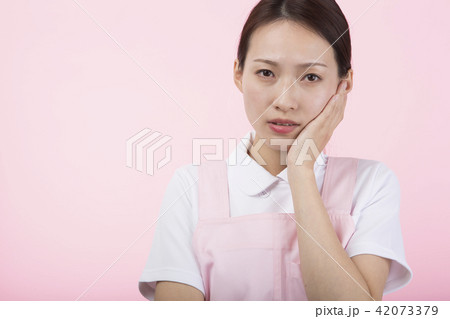 頬に手を当てて困った表情をする白衣とエプロンを着た女性 42073379