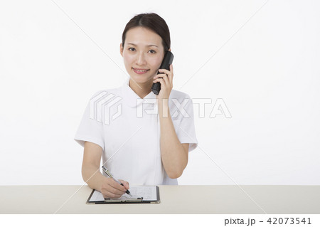 電話の受話器を耳に当てながらメモをとる白衣を着た女性 42073541