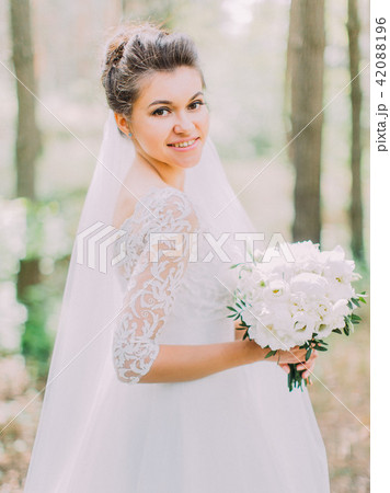 Half-length portrait of the cheerful bride with the wedding bouquet of peonies. The forest location. Half-length portrait of the cheerful bride with the wedding bouquet of peonies. The forest location. 42088196