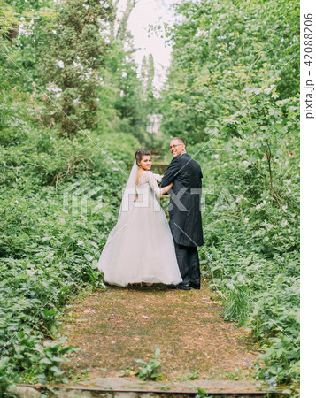 Walking newlywed couple along the road surrounded by green bushes. Walking newlywed couple along the road surrounded by green bushes. 42088206