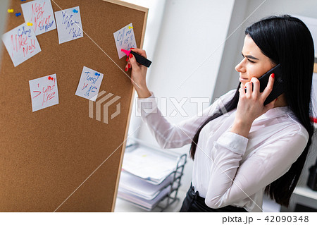 A young girl is talking on the phone, holding a marker in her hand and standing near the board with A young girl is talking on the phone, holding a marker in her hand and standing near the board with 42090348