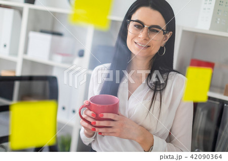 A young girl stands near a board with stickers and holds a red cup in her hands. A young girl stands near a board with stickers and holds a red cup in her hands. 42090364