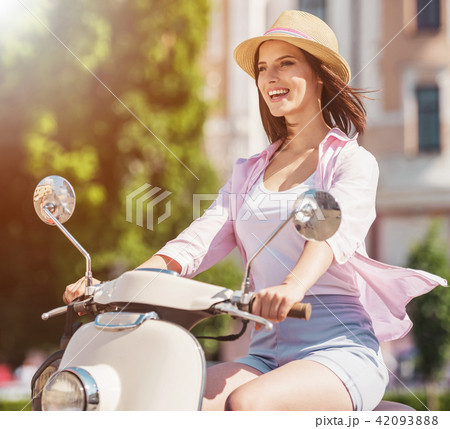 Cheerful Cute Woman Riding Scooter in Summer City. 42093888
