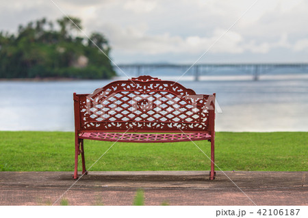 Empty bench, ocean, green grass, cloudy sky 42106187