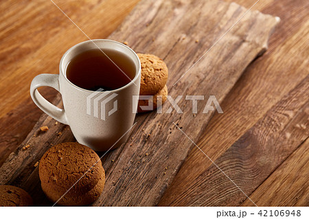 White porcelain mug of tea and sweet cookies on piece of wood over wooden background, top view White porcelain mug of tea and sweet cookies on piece of wood over wooden background, top view 42106948