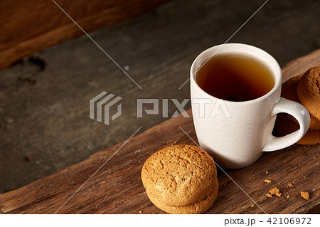 White porcelain mug of tea and sweet cookies on piece of wood over wooden background, top view White porcelain mug of tea and sweet cookies on piece of wood over wooden background, top view 42106972