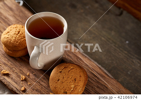 White porcelain mug of tea and sweet cookies on piece of wood over wooden background, top view White porcelain mug of tea and sweet cookies on piece of wood over wooden background, top view 42106974