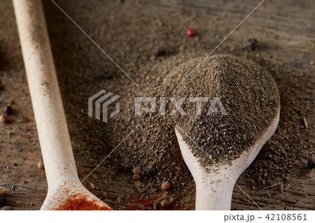 Top view of a wooden spoon full of black pepper on wooden barrel background, selective focus. 42108561