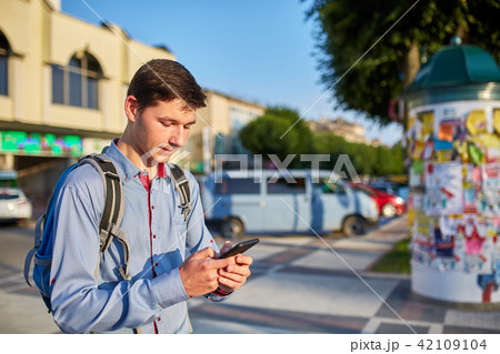 A smiling young man with a smartphone in his hands walking around the city on the background of 42109104