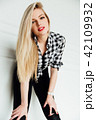 beautiful young blond woman posing while leaning on interior studio wall. 42109932