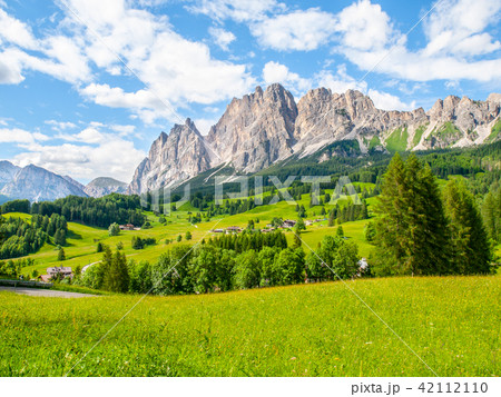 Rocky ridge of Pomagagnon Mountain above Cortina d'Ampezzo with green meadows and blue sky with 42112110
