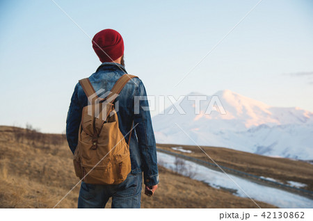 Bearded tourist hipster man in a hat with a backpack stand back on a roadside bump and watching the 42130862