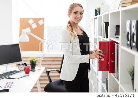 A young girl stands near a rack in the office and takes out a folder. A young girl stands near a rack in the office and takes out a folder. 42135371