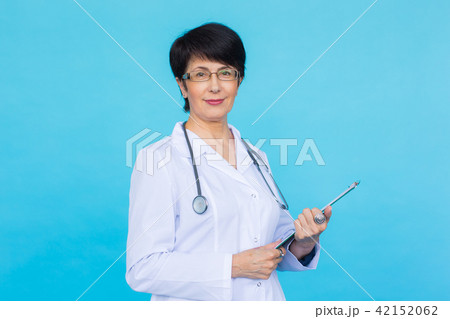 Portrait Of Female Doctor Writing On Clipboard Over a blue background Portrait Of Female Doctor Writing On Clipboard Over a blue background 42152062