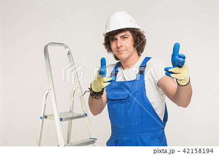 Portrait of handsome builder in white helmet pointing on camera and standing infront of a stairway. 42158194