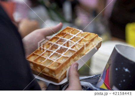 Belgian fresh warm waffle with powdered sugar in hands of buyer. Gastronomic dainty products on 42158443