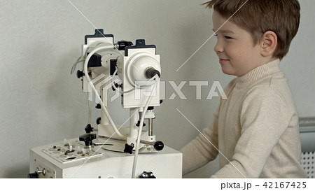 Old male doctor examines eyes of boy through slit lamp Old male doctor examines eyes of boy through slit lamp 42167425