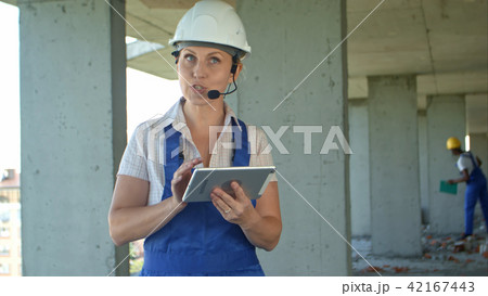 Female construction engineer reading plans using digital tablet and talk to workers through internal 42167443