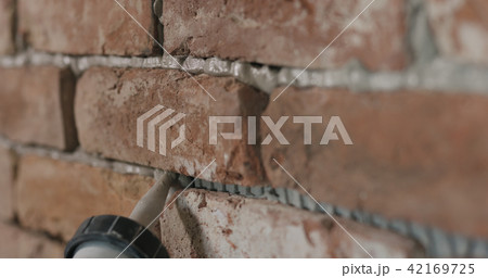 Slow motion closeup of worker filling seam between bricks with mortar from sealant gun 42169725