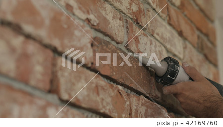 Slow motion closeup of worker filling seam between bricks with mortar from sealant gun 42169760
