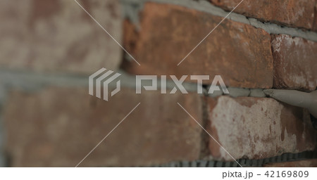 Slow motion closeup of worker filling seam between bricks with mortar from sealant gun 42169809