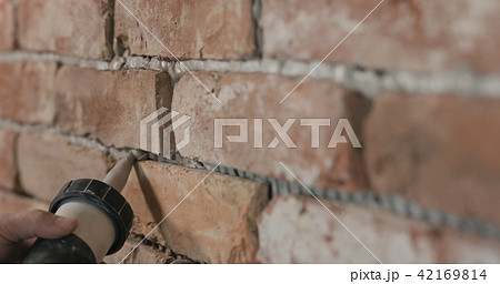 Slow motion closeup of worker filling seam between bricks with mortar from sealant gun 42169814