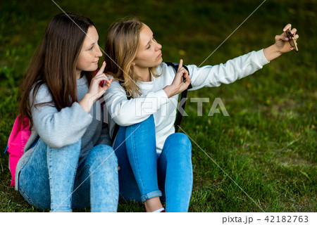 Two girl schoolgirl girlfriends. In summer they sit on grass. In his hand holds a smartphone 42182763