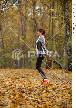 Full-length picture of young brunette jumping with rope at autumn forest 42183494