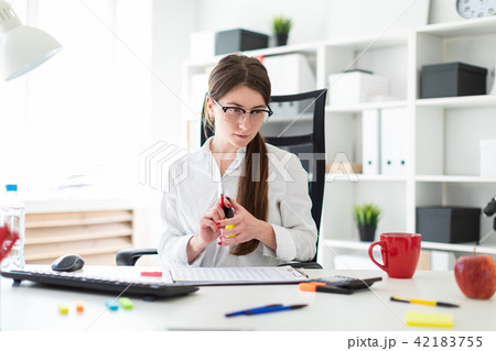 A young girl is sitting at a table in the office, holding a pencil in her hand, a marker and working A young girl is sitting at a table in the office, holding a pencil in her hand, a marker and working 42183755