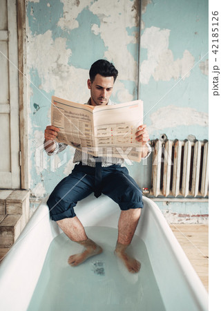 Businessman sitting in bathtub and reads newspaper 42185126