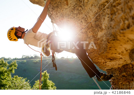 Image of male climber in helmet clambering up cliff. 42186846