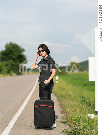 Woman with luggage hitchhiking along a road 42192184