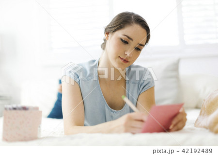 Woman writing in card on bed Woman writing in card on bed 42192489