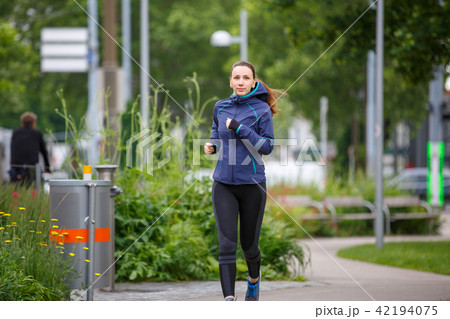 Young woman in blue jacket jogging in park 42194075