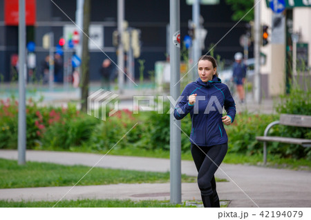 Young woman in blue jacket jogging in park 42194079