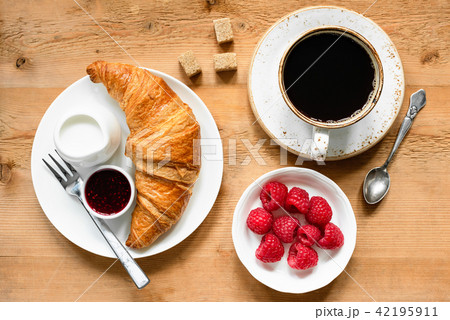 Croissant, black coffee, raspberries and jam on wooden table Croissant, black coffee, raspberries and jam on wooden table 42195911