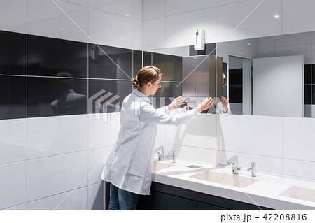 Cleaning woman refilling paper towels in public toilet  Cleaning woman refilling paper towels in public toilet  42208816