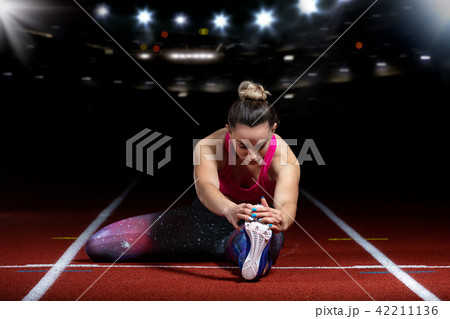 young athletic woman doing exercises on flexibility. stretching legs sitting track stadium, night young athletic woman doing exercises on flexibility. stretching legs sitting track stadium, night 42211136