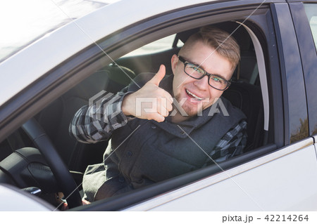 Cheerful casual guy smiling happily showing thumbs up sitting in a big white car 42214264