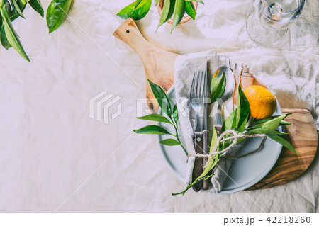 Table setting with white plate, cutlery, linen napkin and orange tree branch decoration on white 42218260