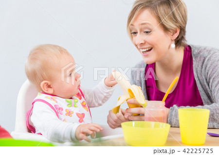 happy mother giving a fresh and nutritious banana to her cute baby girl 42225725