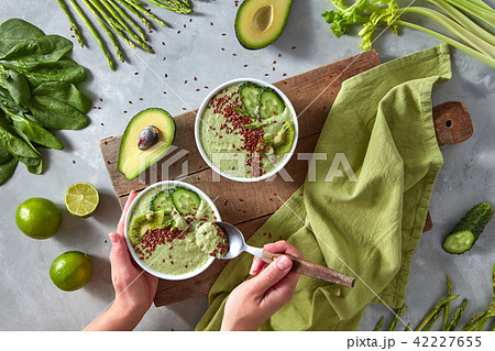 Organic fresh smoothies from green vegetables in a plate on a wooden board on a gray kitchen counter Organic fresh smoothies from green vegetables in a plate on a wooden board on a gray kitchen counter 42227655