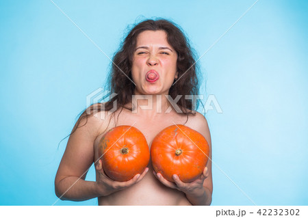 Breasts implant concept - Happy woman holding two pumpkins in front of her breasts 42232302