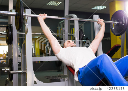 Sport, fitness, training and people concept - Muscular man doing heavy exercise pumping up muscles Sport, fitness, training and people concept - Muscular man doing heavy exercise pumping up muscles 42233153